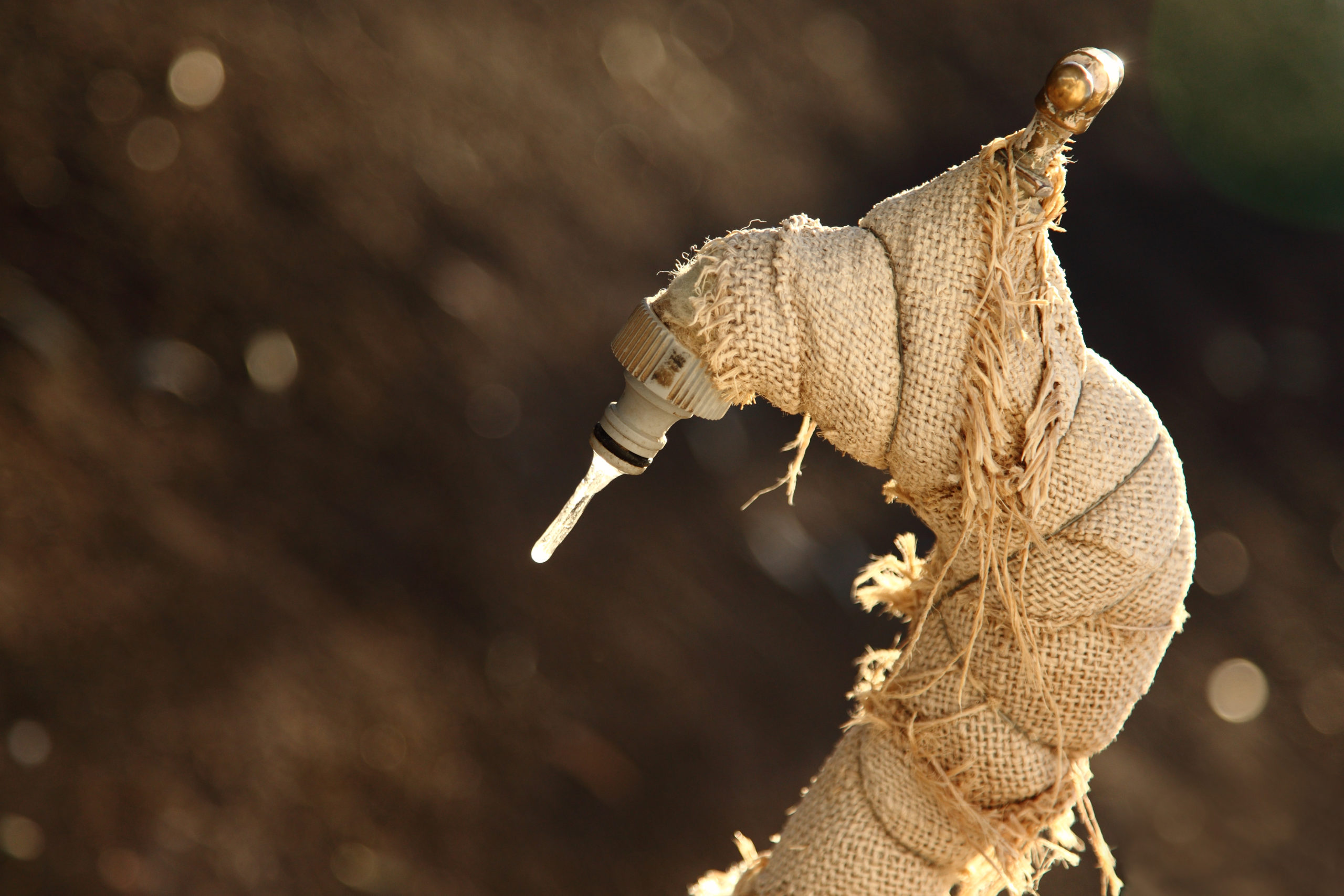 Outdoor faucet covered in burlap with frozen drip